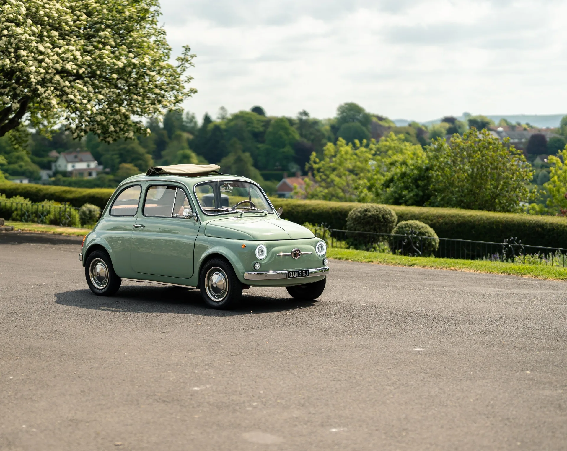 Mint green classic Fiat 500 parked under a tree on a countryside lane